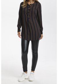 Svart och brunrandig lång tunika med knapplist, kombinerad med glänsande svarta leggings och kraftiga vita sneakers.