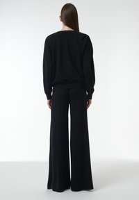 Zwarte gebreide trui met een brede halslijn en geribbelde manchetten, gecombineerd met zwarte high-waisted wijde broekspijpen. Zachte, gladde textuur.