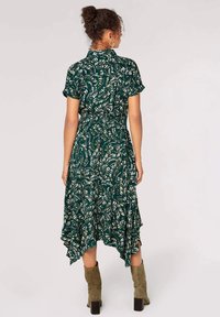 Groene jurk met bladenprint, korte mouwen, cinched taille en asymmetrische zoom. Gecombineerd met olijfgroene enkelboots.