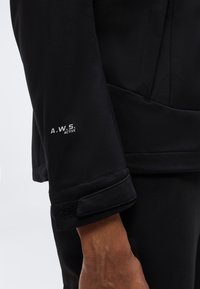 Κοντινό πλάνο του μανικιού ενός μαύρου μπουφάν με ρυθμιζόμενο μανσέτα βέλκρο και κείμενο «A.W.S. Active» στο μπροστινό μέρος του βραχίονα.