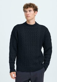 Pull en tricot sombre présentant un motif de câble texturé, un col ras du cou côtelé et des manches longues. Fabriqué en tissu doux et épais.