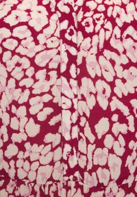 Roter Stoff mit einem weißen und hellrosa abstrakten Muster, das in der Mitte eine Knopfleiste und eine strukturierte Oberfläche aufweist.