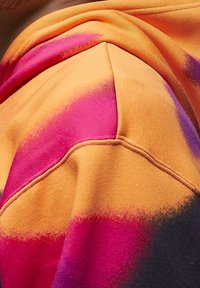 Felpa con cappuccio in tessuto arancione con accenti sfumati in rosa e viola. Superficie testurizzata con cuciture visibili e vestibilità comoda.