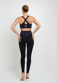 Bra sportivo nero con spalline incrociate, caratterizzato da un'apertura e una vita a pois colorati. Leggings neri aderenti con dettagli laterali.