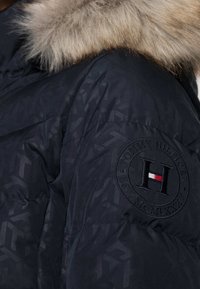 Granatowa kurtka puchowa z odpinanym futrzanym kołnierzem, z okrągłą naszywką z logo "Tommy Hilfiger" i geometrycznym detalem tekstury.