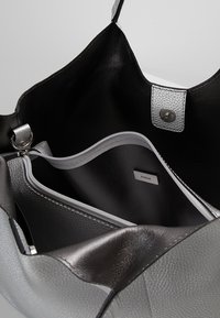 Grijze en zwarte leren handtas met textuur, een ruime binnenkant, een ritsvak en zilveren hardware. Bevat een logotag aan de binnenkant.