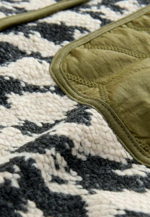 Material texturat în crem, negru și verde măslinie, prezentând o suprafață pufoasă cu o margine netedă, quiltuită în verde măslinie și detalii de cusătură.