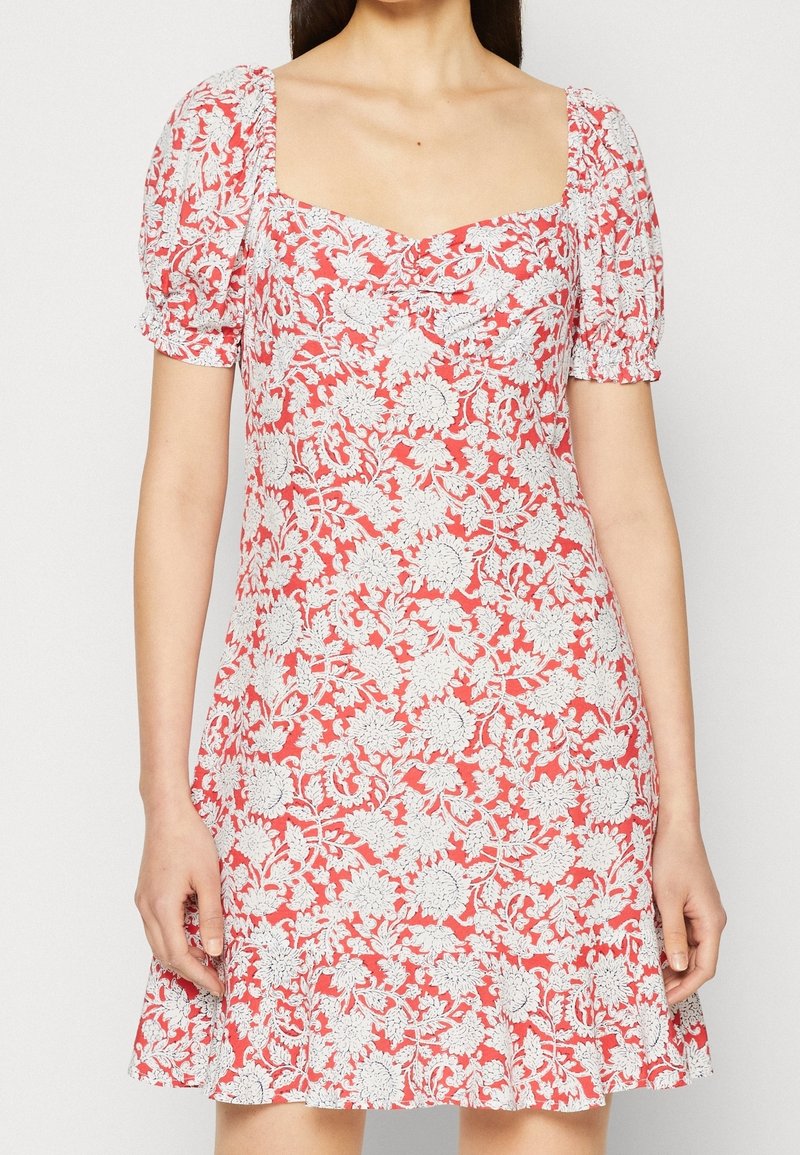 Červené květované šaty s bílými složitými vzory, čtvercovým výstřihem, nabíranými krátkými rukávy a rozšířeným lemem. Vyrobeno z lehké látky.