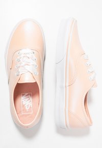 Różowe płócienne trampki w odcieniu różu brzoskwiniowego z białymi gumowymi podeszwami, ozdobione satynowymi sznurowadłami i subtelnymi szwami. Klasyczny, niski fason.