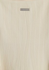 Tissu crème texturé avec des lignes verticales en relief, accentué par une petite étiquette en argent avec "aimn" gravé. Surface douce avec un léger éclat.