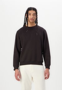 Sort bomulds sweatshirt med rund hals, lange ærmer og ribbede manchetter. Glat tekstur og afslappet pasform, parret med lyse bukser.