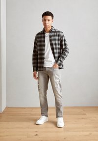 Plaid button-down shirt in black and gray, worn over a white t-shirt. Light gray distressed jeans and white sneakers complete the look.