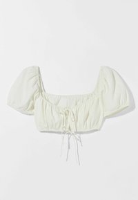 Avkortad blus med fyrkantig halsringning i ljus krämfärgad tyg. Har puffärmar, rynkad midja med knyt-detalj och lätt textur.