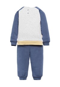 Conjunto de dos piezas para niño pequeño con pantalones azules y una camiseta blanca con mangas azules y cinturilla beige, exhibido sobre un fondo blanco.