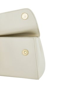 Bolso de mano beige claro con solapa abierta, mostrando cierres magnéticos dorados y detalles de costura visibles en cuero liso.