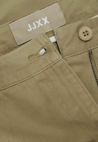 Chinos de algodón beige con cremallera, cierre frontal con botón, presillas para el cinturón y la etiqueta de la marca "JJXX" cosida en la cinturilla.