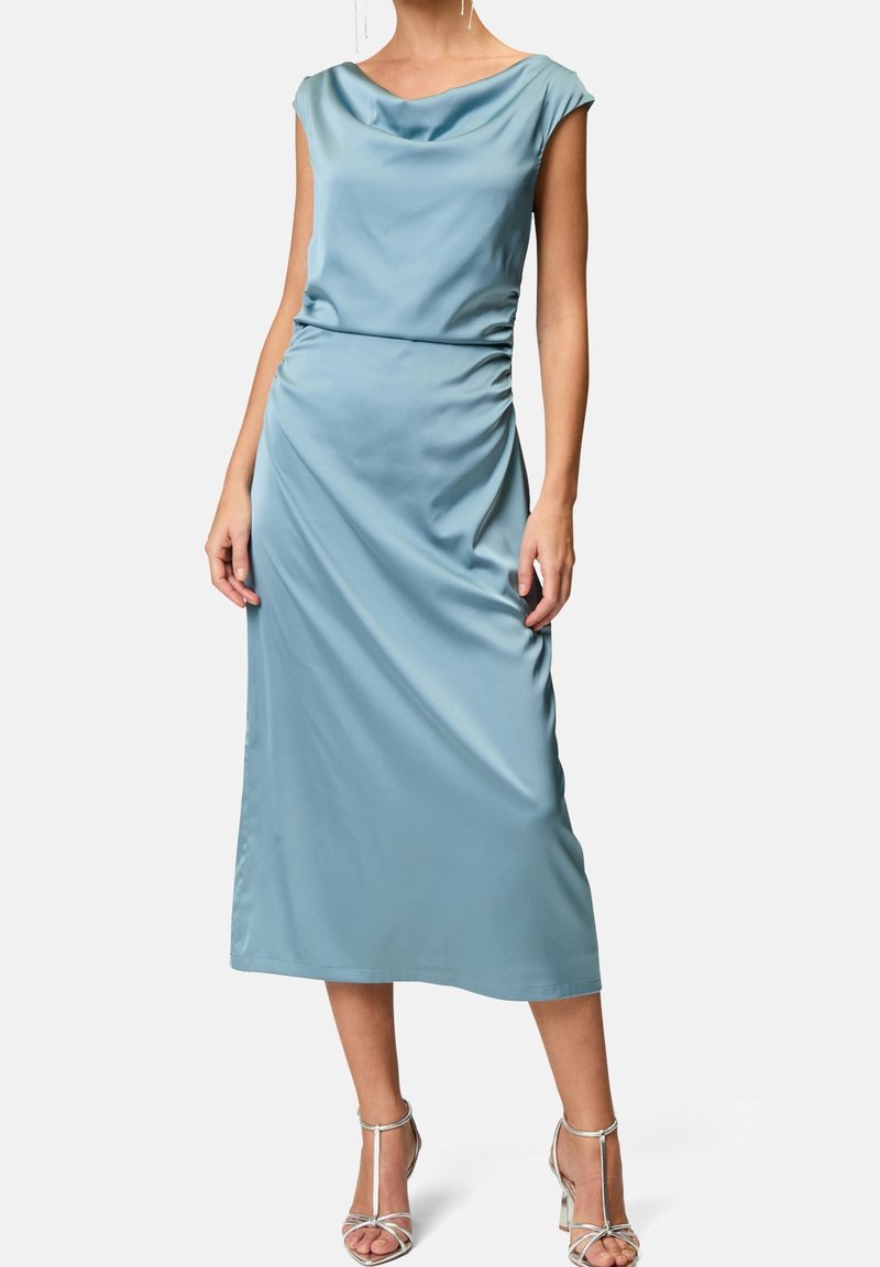 Abito midi in satin blu pastello con scollo a barchetta, maniche corte e dettagli arricciati in vita. Abbinato a tacchi metallici con cinturini.