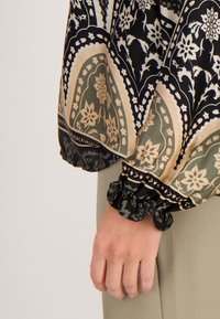 Langarm blouse met een bloemmotief in tinten groen, zwart en beige, voorzien van gathered manchetten en een vloeiende silhouet.