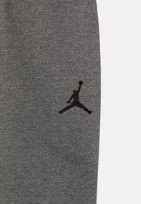 Pantalones de chándal grises con textura suave, que presentan un logotipo de Jumpman bordado en negro en la parte inferior de la pierna izquierda.