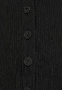 Gros plan sur un tissu en maille côtelée noire avec quatre boutons ronds noirs, chacun gravé du texte « Marco Polo Denim ».