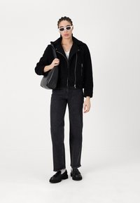 Zwarte tekstuurjacket, witte zonnebril, zwarte schoudertas, grijs T-shirt, zwarte jeans, zwarte schoenen met dikke zolen, staand op een witte achtergrond.