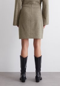 Robe en tricot vert olive avec une taille cintrée, des manches longues et une fermeture éclair au dos ; assortie avec des bottes en cuir noir montantes à talon épais.