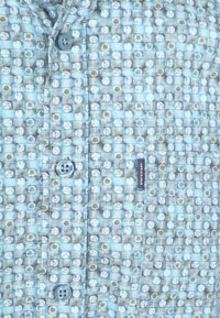 Musterhemd in Blau mit einem Karodesign und kleinen weißen und braunen Blumenmotiven. Enthält hellblaue Knöpfe und ein Etikett.