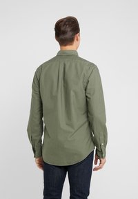 Vihreä pitkähiha paita, jossa on klassinen kaulus, nappirannekkeet ja suora leikkaus. Kangas näyttää pehmeältä ja sileältä.