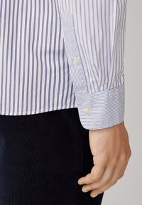 Camicia a righe blu chiaro e bianca con polsi abbottonati, realizzata in tessuto liscio. Presenta strisce verticali sottili e una tasca.