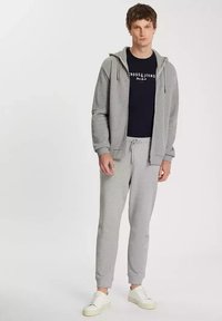 Szary hoodie z zamkiem z przodu, bocznymi kieszeniami i sznurkiem. Połączony z dopasowanymi szarymi joggerami i białymi sneakersami. Pod spodem znajduje się ciemna koszulka.