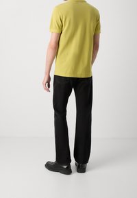 T-shirt en coton jaune vif à manches courtes, associé à un jean en denim noir et des chaussures noires, vu de dos. Design simple, sans motifs.