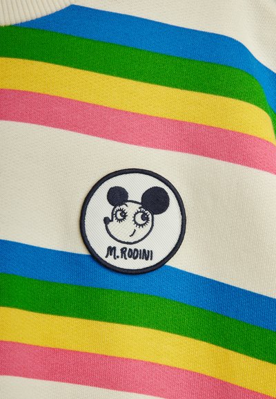 Ύφασμα με ρίγες σε χρώματα του ουράνιου τόξου με στρογγυλό λευκό σήμα που απεικονίζει ένα στυλιζαρισμένο πρόσωπο ποντικιού και το κείμενο "M. Rodini" κεντημένο με μαύρο χρώμα.