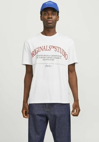 Hvid bomulds t-shirt med rød grafisk tekst. Rund hals, korte ærmer og en afslappet pasform. Kombineret med mørke denimjeans.