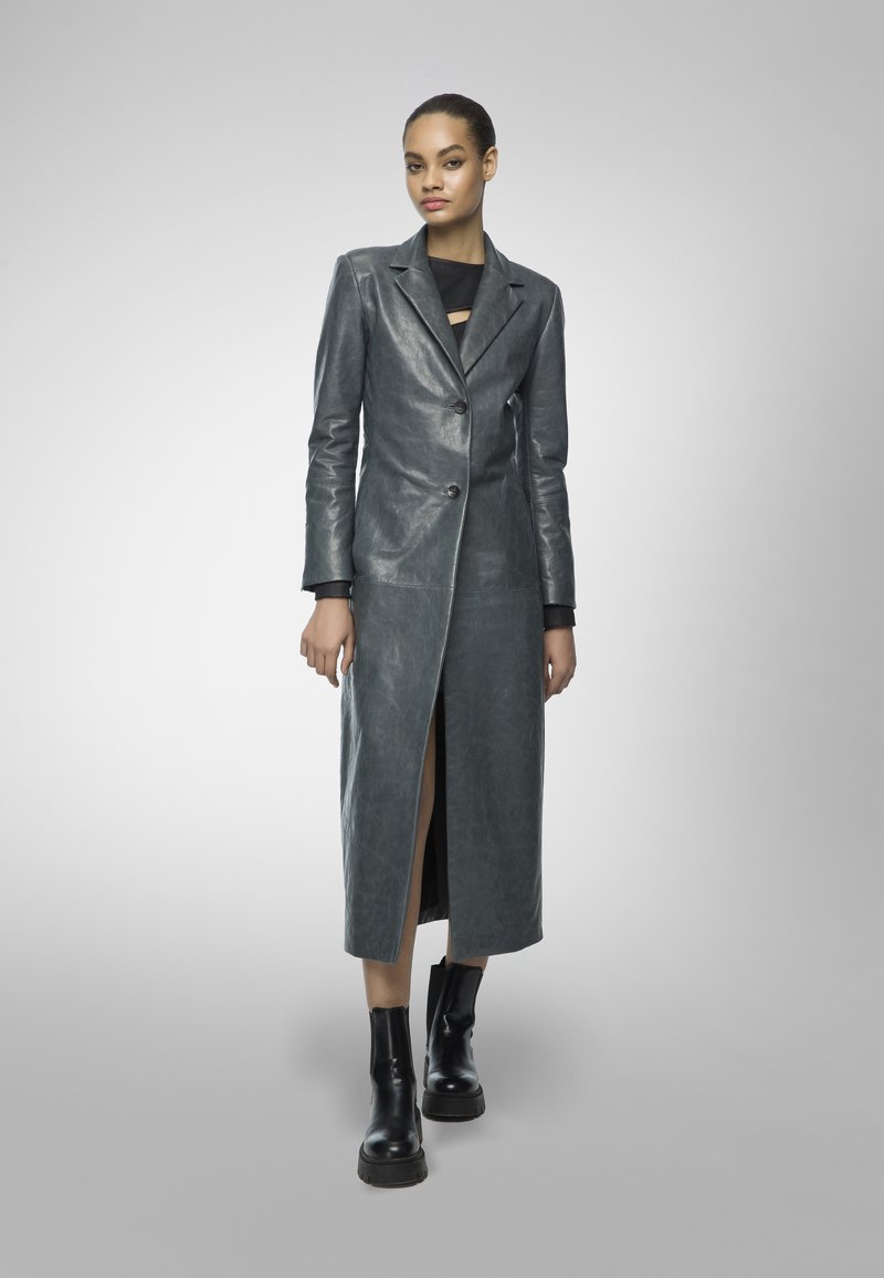 Long, grey leather coat with a single button closure and a deep side slit, paired with black ankle boots and a fitted black top.