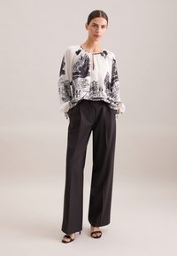 Camicia bianca a maniche lunghe con stampa architettonica nera; abbinata a pantaloni neri a vita alta e sandali neri con tacco.