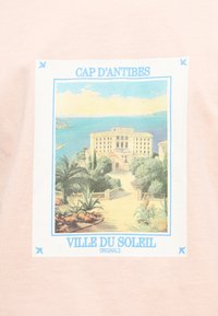 Κτίριο στον ηλιόλουστο ακρωτηριακό χώρο με θέα στη θάλασσα, περιτριγυρισμένο από δέντρα και φυτά, με τα κείμενα "Cap d'Antibes" και "Ville du Soleil" πάνω και κάτω αντίστοιχα.