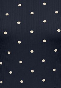 Granatowa prążkowana tkanina z nieregularnymi kremowymi kropkami. Charakteryzuje się teksturowaną powierzchnią i równomiernie rozmieszczonym wzorem kropek.