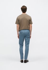 Καφέ βαμβακερό μπλουζάκι με κοντά μανίκια, συνδυασμένο με ανοιχτό μπλε ραμμένο παντελόνι και καφέ δερμάτινα παπούτσια, σε θέα από πίσω.