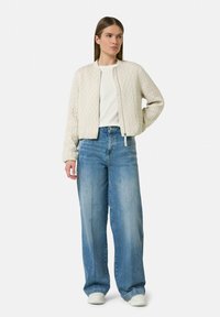 Quilted cream bomber jacket with ribbed cuffs, paired with light blue wide-leg jeans. Simple white T-shirt underneath.