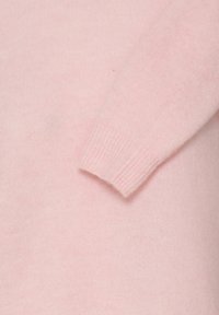 Manche de pull en maille rose douce avec poignet côtelé visible sur un fond de tissu rose assorti.