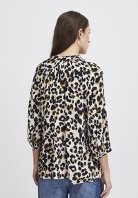 Top s leopardím vzorom z ľahkého materiálu, so skladaným chrbtom, trojštvrťovými rukávmi a voľným strihom. Predovšetkým čierne, béžové a zlaté odtiene.