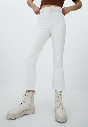 White, high-waisted pants with a flared hem, paired with beige lace-up boots featuring a chunky sole and side zipper details.