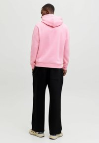 Felpa rosa con cappuccio, tessuto morbido, polsini aderenti e tasca a marsupio, abbinata a pantaloni neri e sneaker beige.