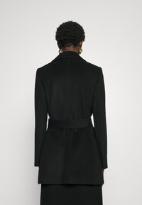 Sorte skræddersyet frakke med bælte i taljen, strukturerede revers og et mellemlangt design. Fremstillet af glat stof, der viser en minimalistisk silhuet.