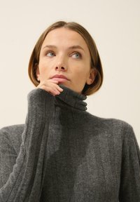 Szary sweter z golfem, wykonany z miękkiego materiału, z wysokim kołnierzem i długimi rękawami, zaprezentowany z naciskiem na dekolt i teksturę.