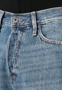 Jeans de denim azul claro con un corte estándar, que cuentan con costuras naranjas y un cierre de botón de metal. Presentados a la altura de la cintura con una textura suave.