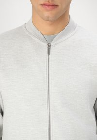 Light gray zip-up jacket with a round collar. Smooth cotton fabric, featuring a metallic zipper and a minimalistic design.