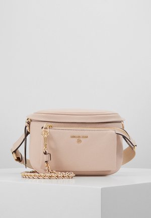 Sac banane beige en cuir Michael Kors avec poche zippée à l'avant, détail chaîne dorée et sangle en tissu réglable sur surface blanche contre un fond gris.