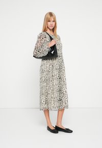 Langes, gemustertes Kleid in Beige und Schwarz mit transparenten Ärmeln; kombiniert mit einer glänzenden schwarzen Handtasche und schwarzen Ballerinas. Glatte Textur und fließendes Design.