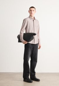 Borsa in pelle nera, con parte superiore arrotolata, indossata con una camicia a fantasia floreale leggera e jeans scuri, completata da scarpe nere. Design e struttura semplici.